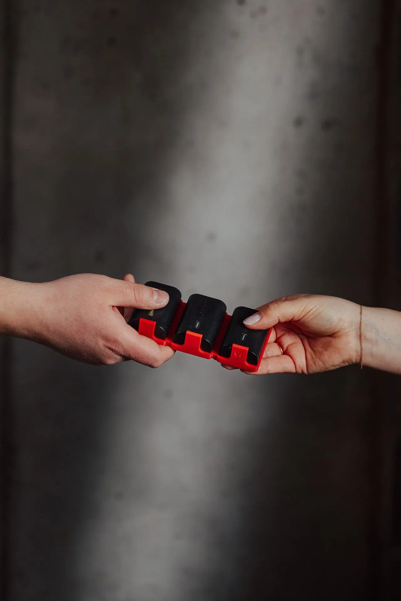 Two people passing a 3d printed Hōld Trio support holding three batteries from one hand to another