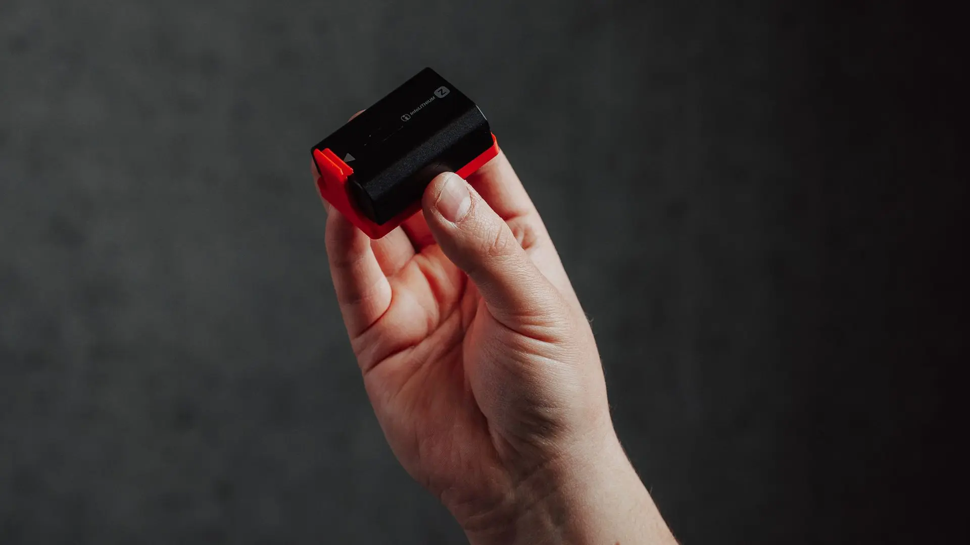 A hand holding the Hōld support with a camera battery inside